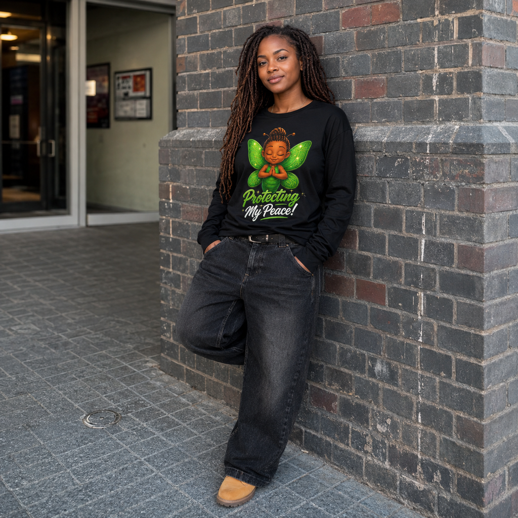 A woman with long dreadlocks stands against a gray brick wall wearing a black long-sleeve graphic t-shirt with a colorful angel design and the text 'Protecting My Peace!'.