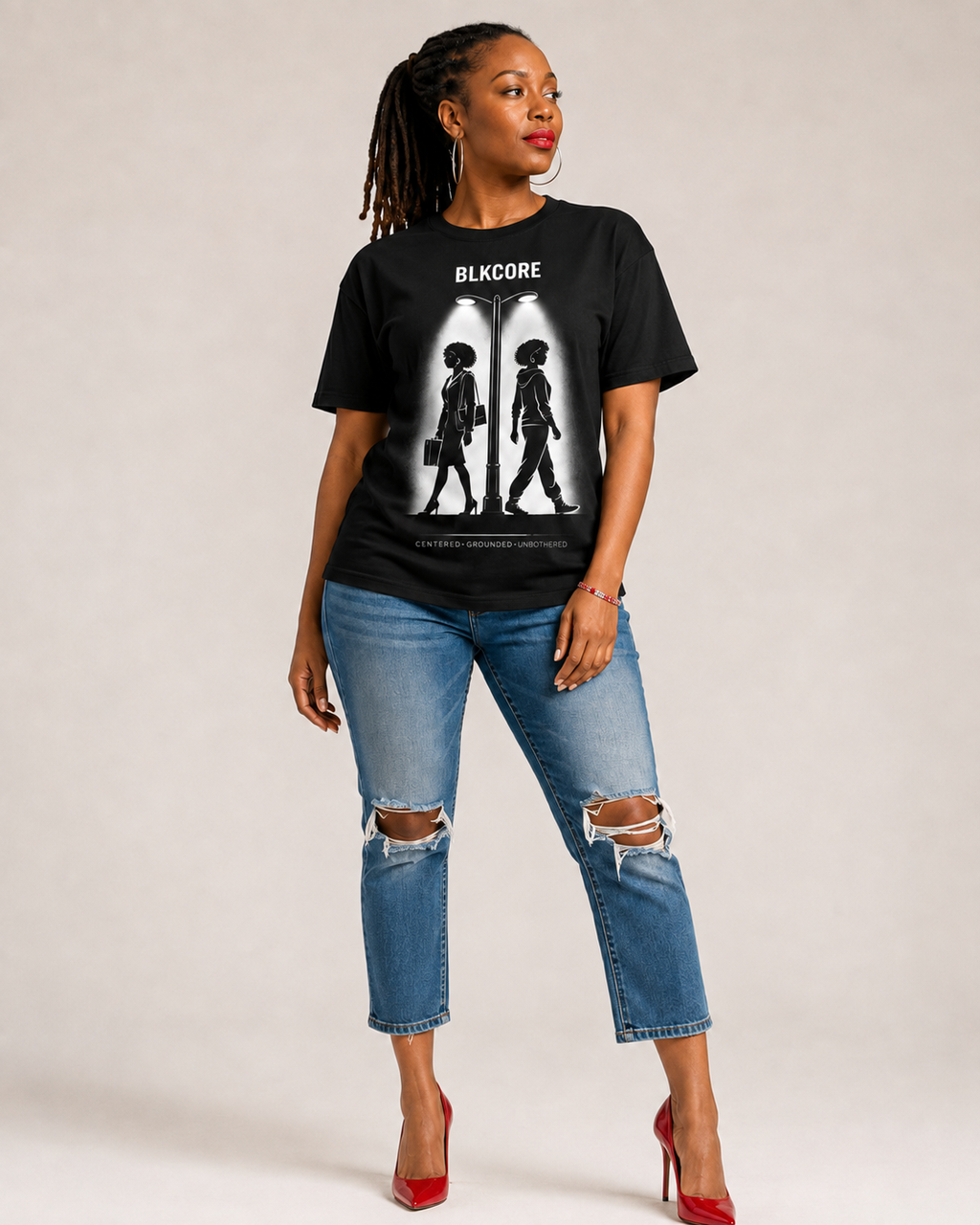 A woman modeling a black graphic t-shirt with the text 'BLKCORE' and a white silhouette print, paired with distressed blue jeans and red high heels, against a light gray studio background.