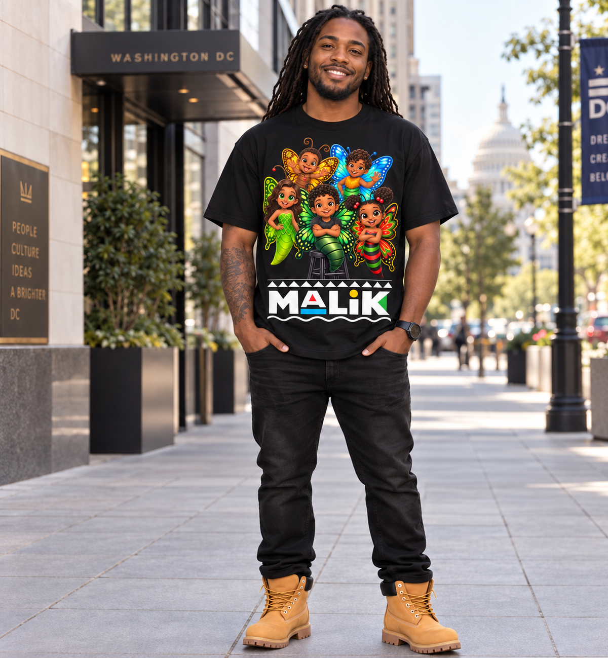 A man stands on a city sidewalk wearing a black graphic T-shirt with a colorful cartoon-style print and the text 'MALIK' across the front, paired with black pants and tan boots. The background shows a Washington DC urban setting with buildings and street elements.